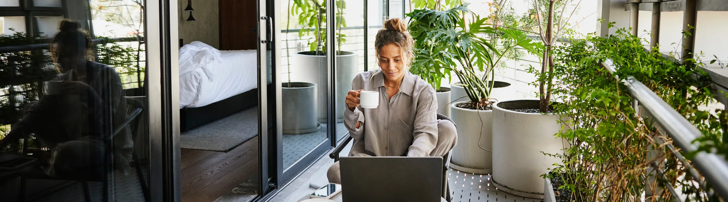 a remote worker with business travel insurance sits on a hotel balcony with a coffee and a laptop