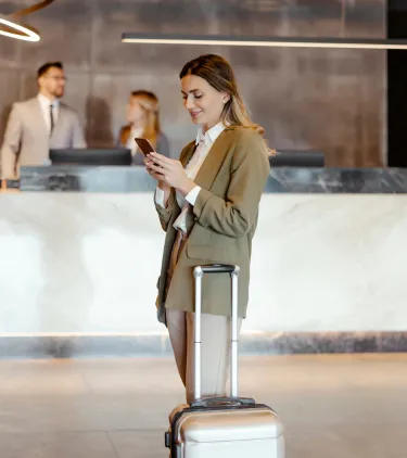 a female traveler looks at her phone as she checks into a hotel, insured with business travel insurance 