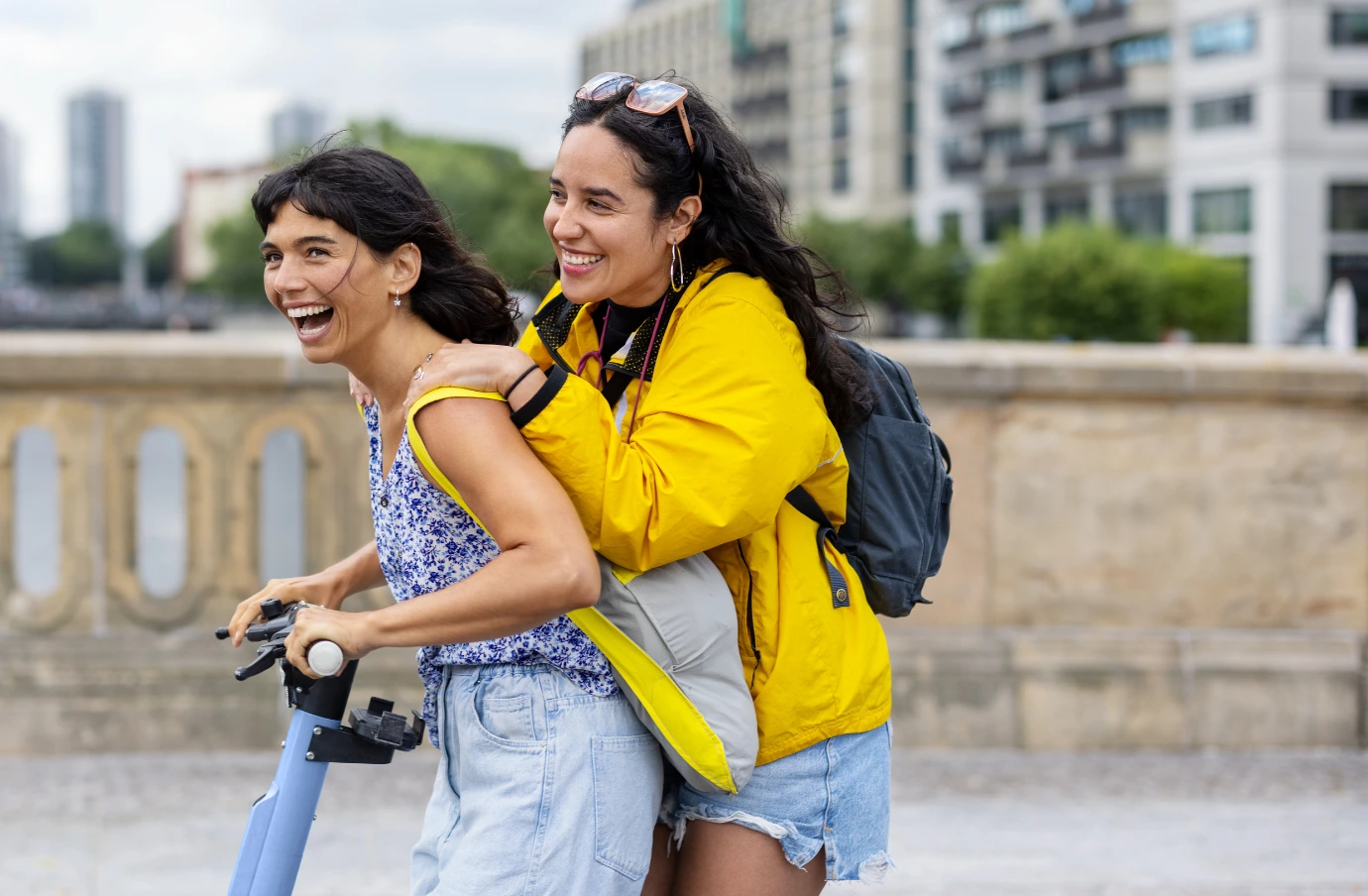 two friends with travel insurance for students ride an electric scooter through a city abroad