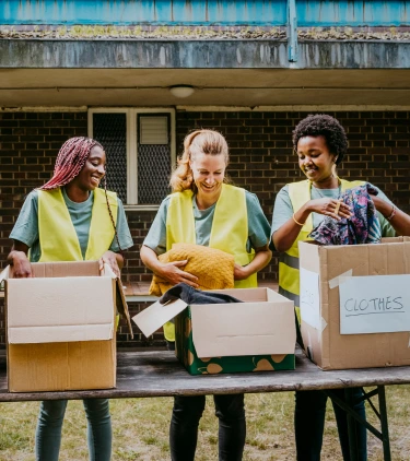 three volunteers sort clothing donations together on their service trip, insured with volunteer travel insurance 