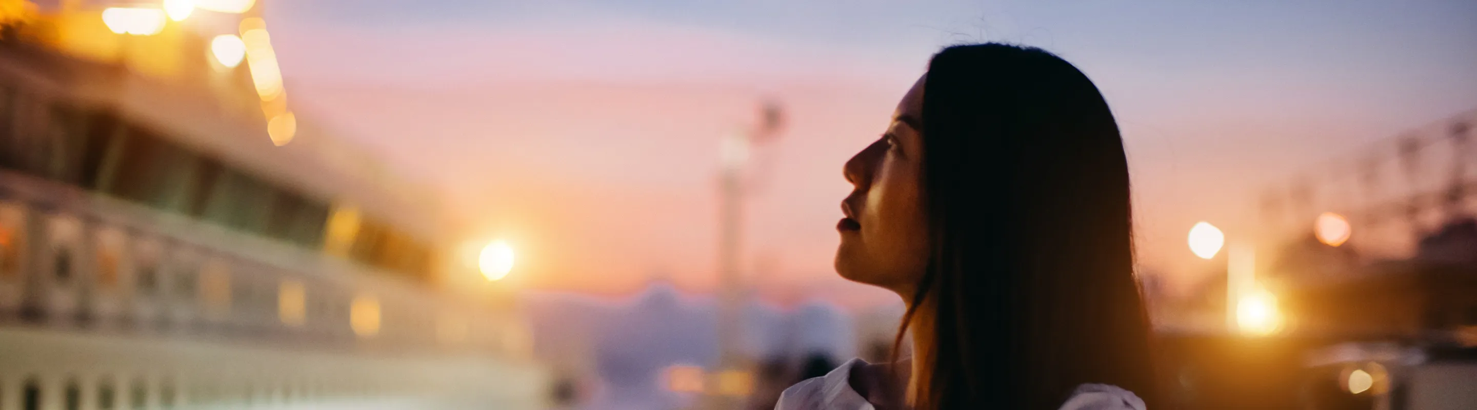 a young woman admires a twinkling cruise ship at sunset, insured with cruise travel insurance 