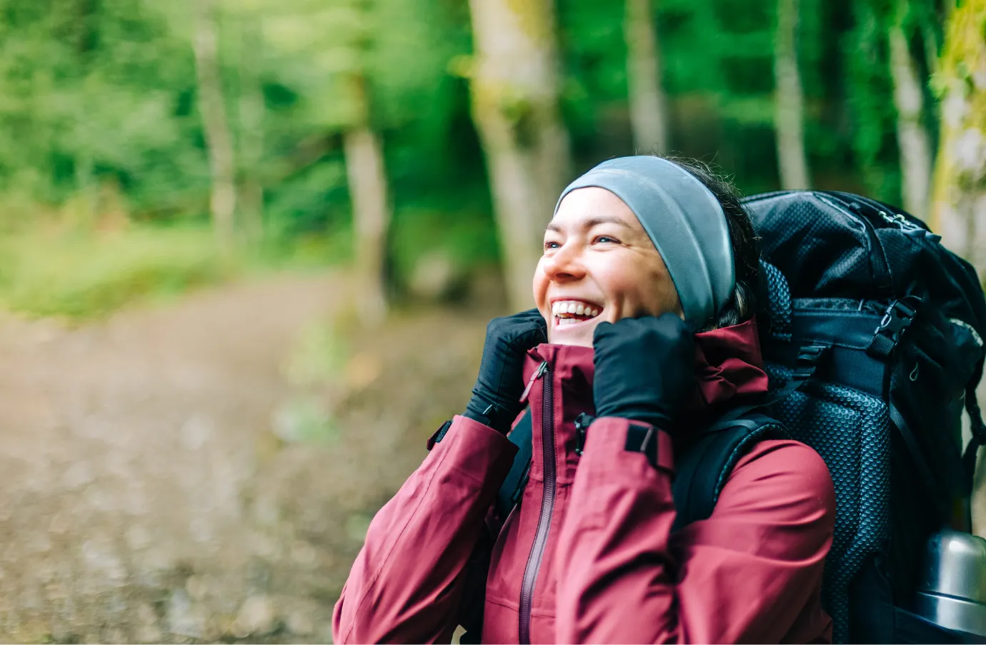 a woman with adventure travel insurance smiles as she hikes with a backpack in the forest 