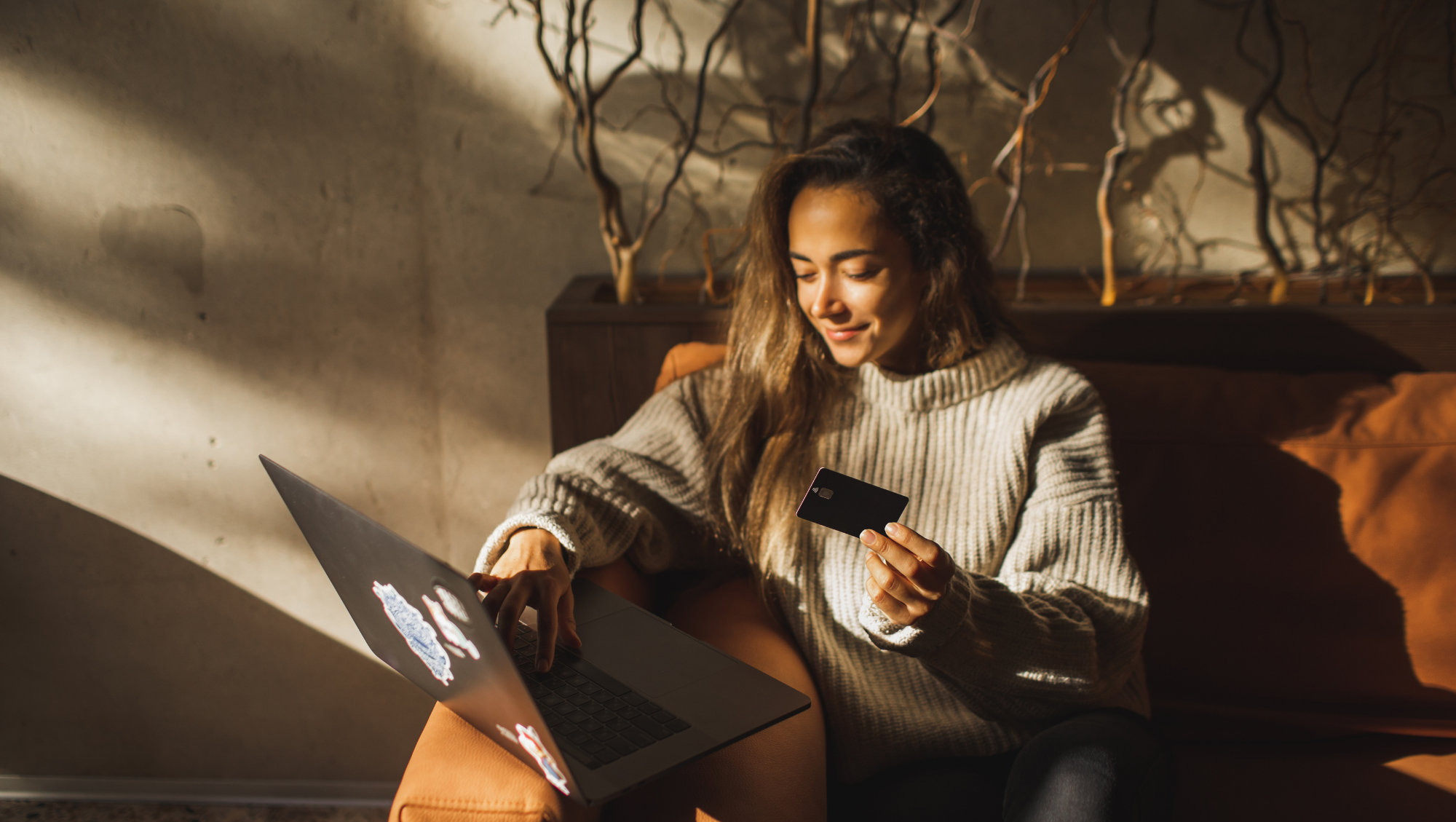 a woman sits on a couch with natural light, holding her credit hard and looking up "How much is travel insurance?"