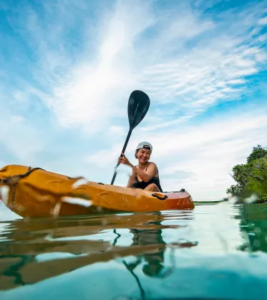 a woman with adventure travel insurance paddles her kayak through a crystal-clear lagoon
