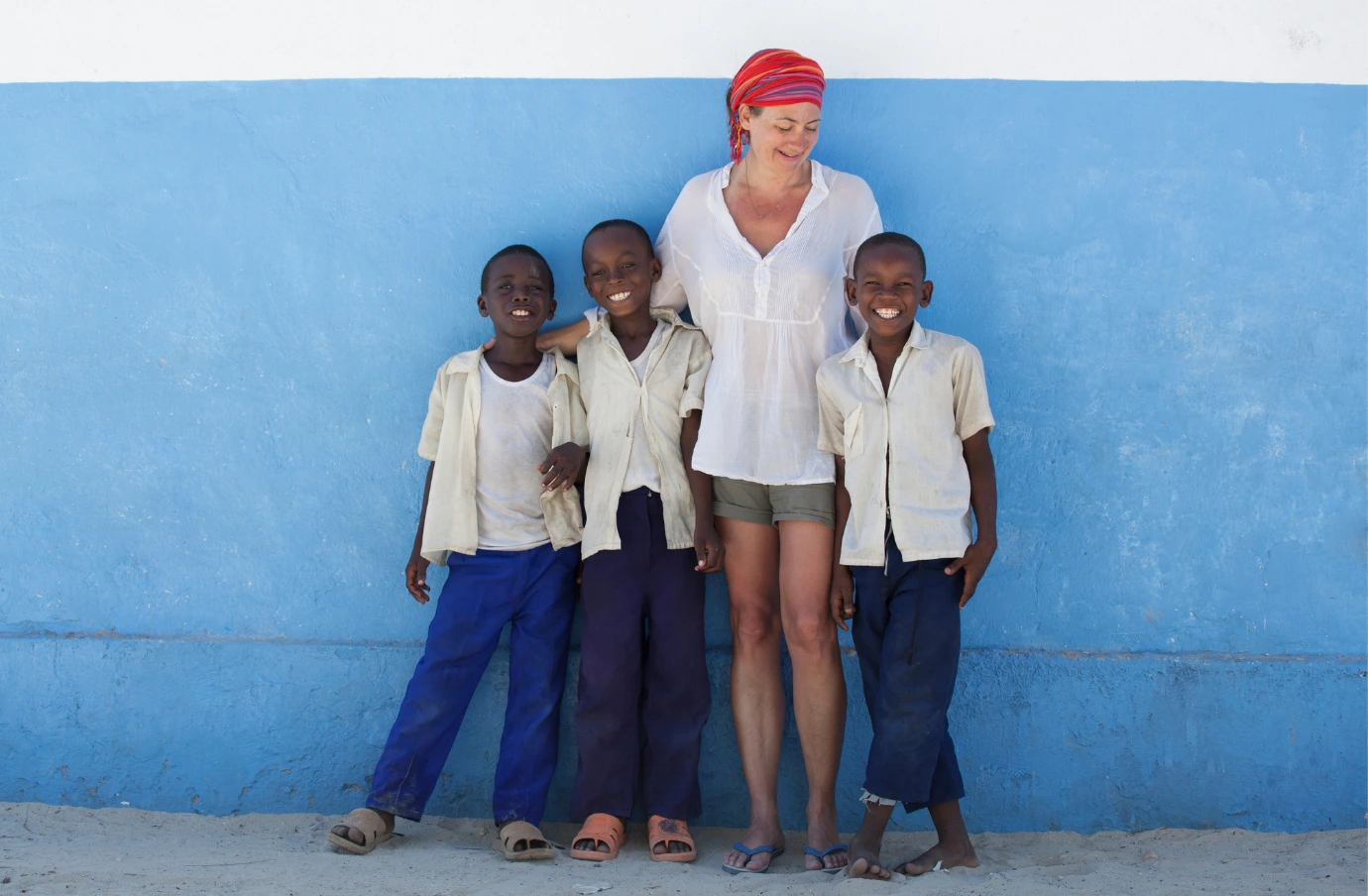 a woman with volunteer travel insurance stands outside with three children in Africa 