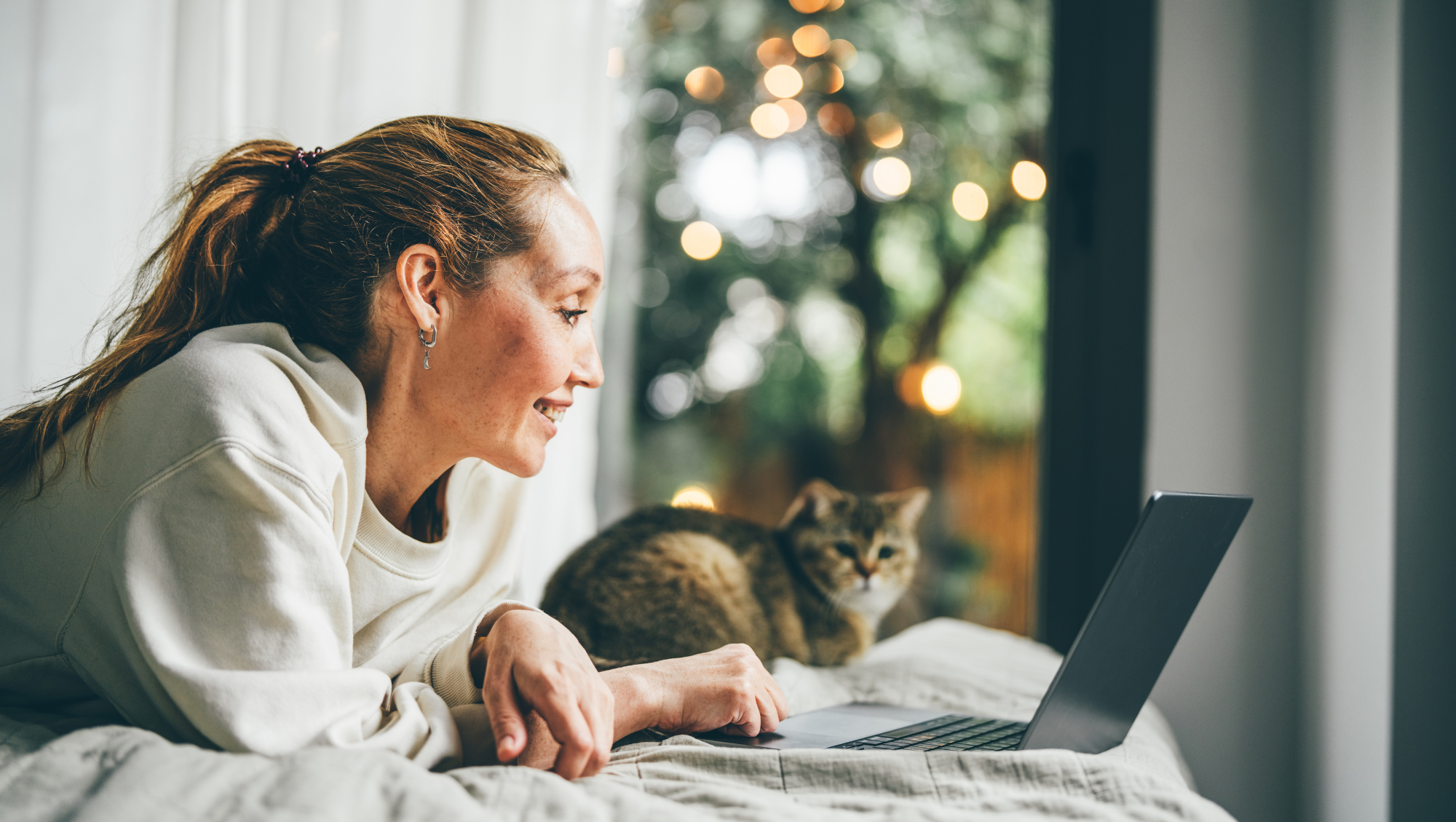 a woman uses her laptop at home with her cat nearby, researching "How much is travel insurance?"