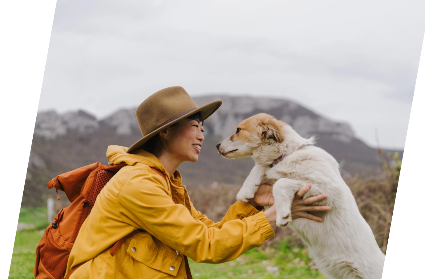 Woman with pet travel insurance holding her dog up to her face with mountains in the background