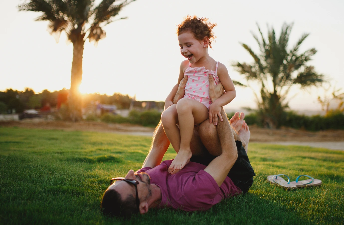 an adult and child play in the grass near palm trees at sunset, insured with travel insurance for Israel