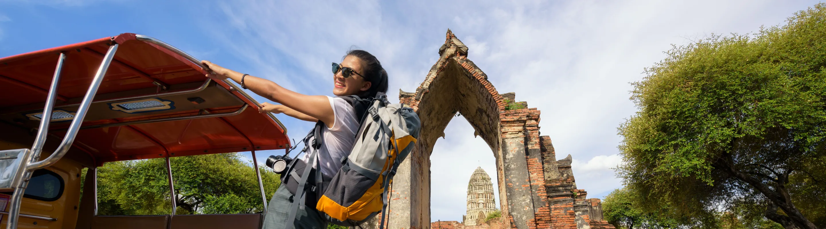 a backpacker with travel insurance for Thailand climbs onto a tuk-tuk beside historic temple ruins in Ayutthaya