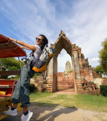 a backpacker with travel insurance for Thailand climbs onto a tuk-tuk beside historic temple ruins in Ayutthaya