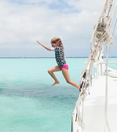 a child with travel insurance for the Bahamas jumps from a sailboat into clear turquoise ocean water