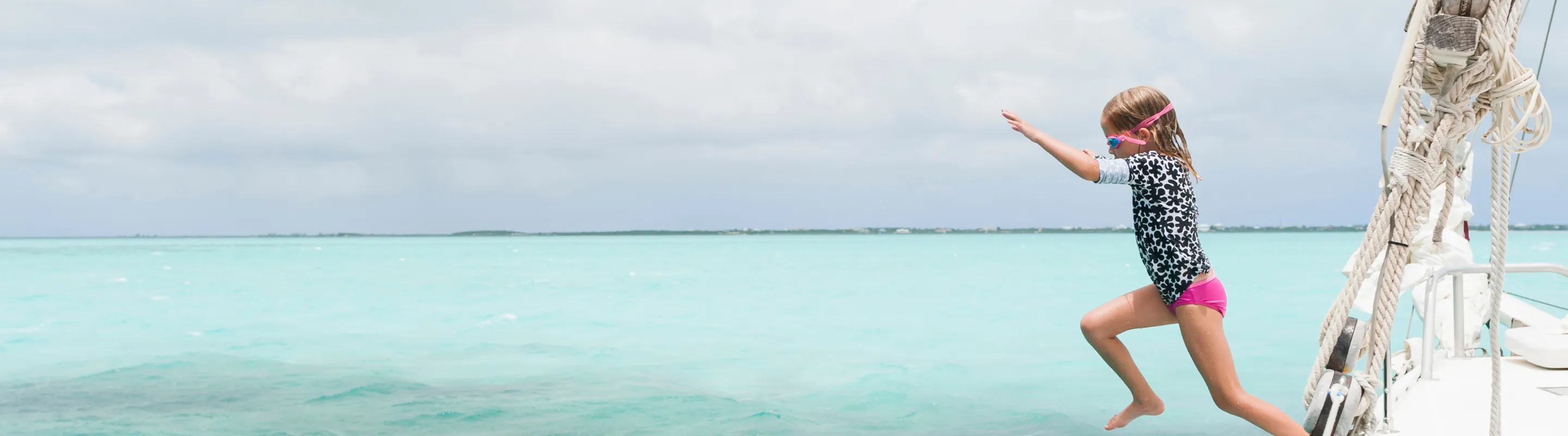 a child with travel insurance for the Bahamas jumps from a sailboat into clear turquoise ocean water