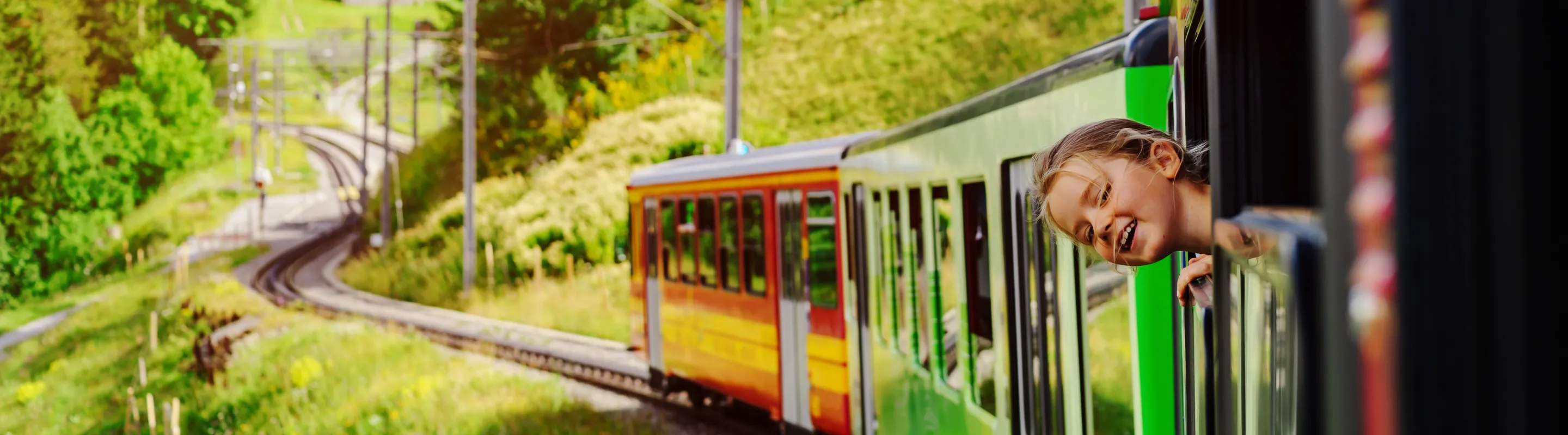 a girl pokes her head out of the window of a colorful train in the Swiss Alps, insured with travel insurance for Switzerland 