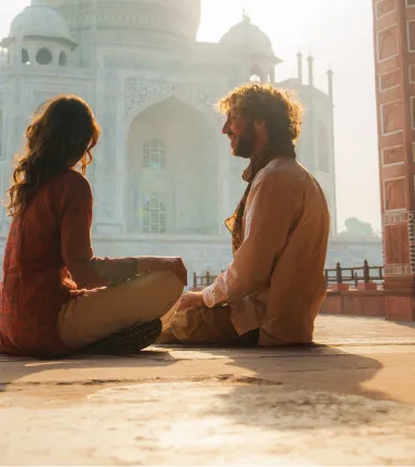 a couple with travel insurance for religious trips admires the Taj Mahal in India at sunrise 