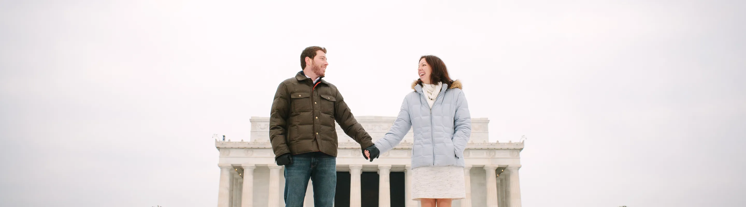 a couple with travel insurance for Washington, D.C. stands hand in hand on the steps in front of the Lincoln Memorial