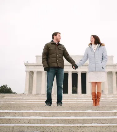 a couple with travel insurance for Washington, D.C. stands hand in hand on the steps in front of the Lincoln Memorial
