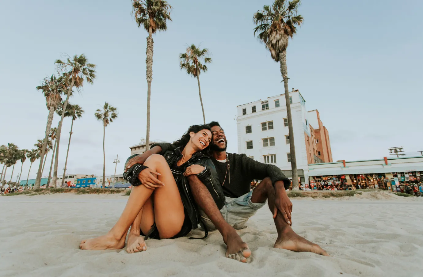 a young couple embraces while sitting at Venice Beach, insured with travel insurance for California