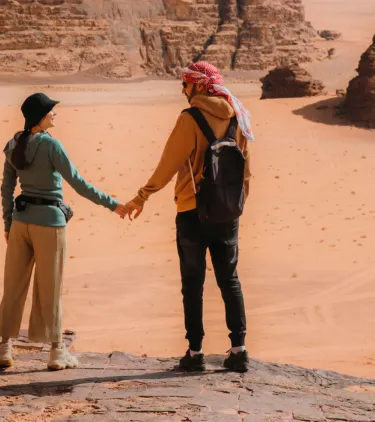 a young couple holds hands on their hike through Wadi Rum Desert, insured with travel insurance for Jordan