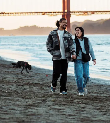 a couple with domestic travel insurance walk along San Francisco's shoreline with the Golden Gate Bridge in the background