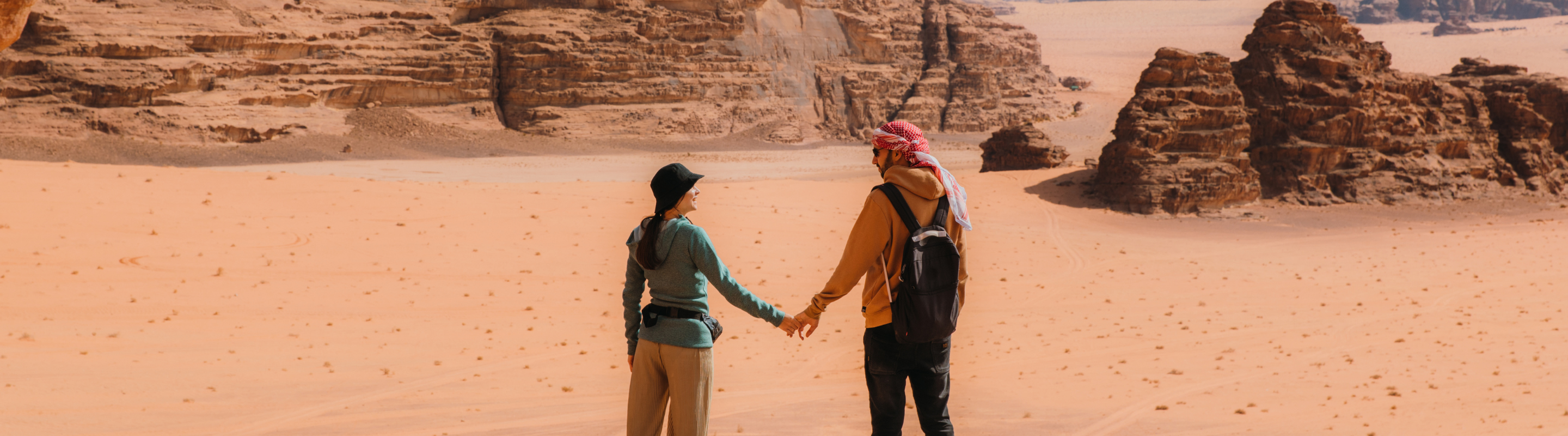 a young couple holds hands on their hike through Wadi Rum Desert, insured with travel insurance for Jordan