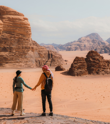 a young couple holds hands on their hike through Wadi Rum Desert, insured with travel insurance for Jordan
