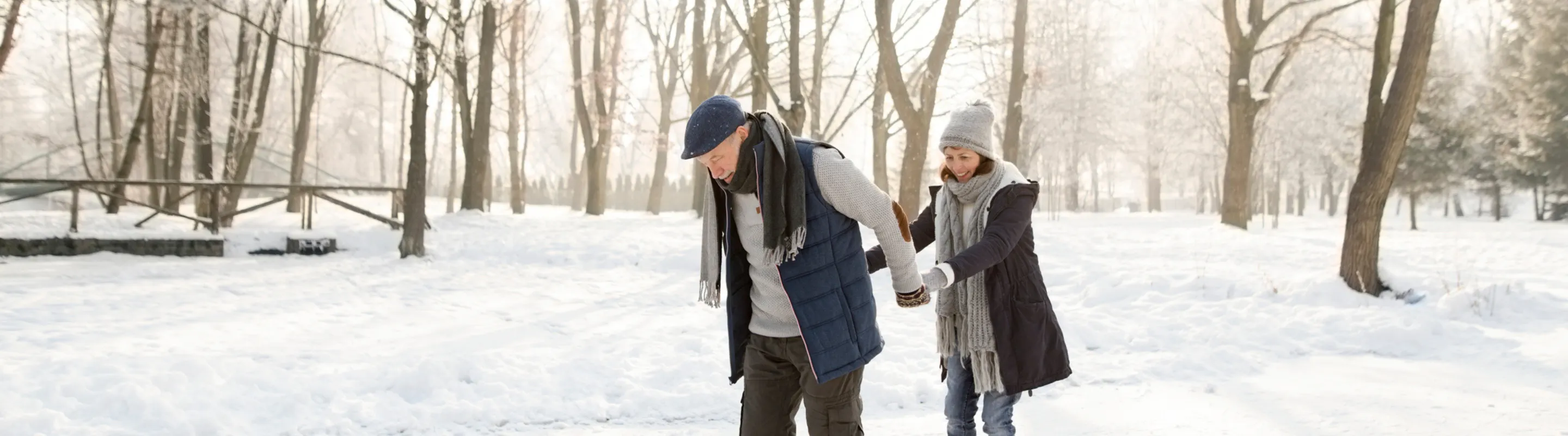 an older couple with ski insurance ice-skate outdoors in a forest setting on their winter trip, insured with ski insurance 