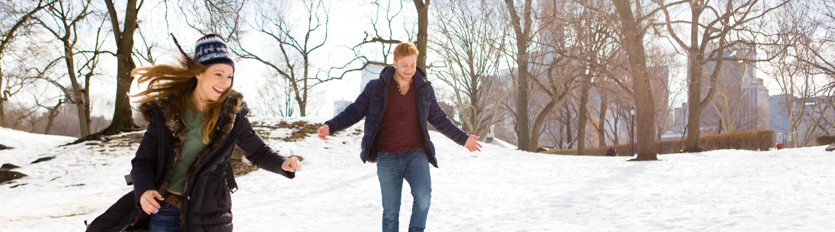 a young couple plays in the snow in Central Park, insured with travel insurance for New York 