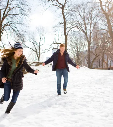 a young couple plays in the snow in Central Park, insured with travel insurance for New York 