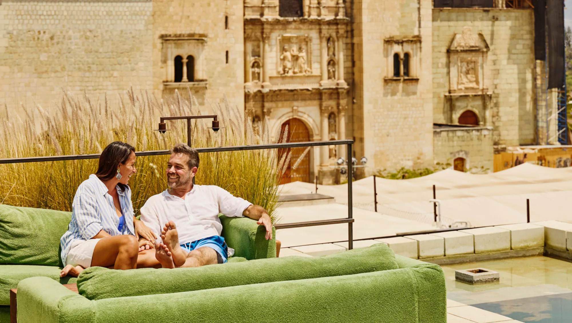a couple with lounges on a rooftop near historic buildings on vacation after asking, "Is it safe to travel to Mexico?"