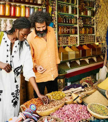 a mixed-race couple shops for spices at a market, insured with travel insurance for Morocco