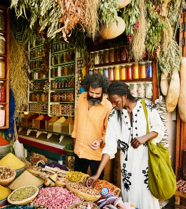 a mixed-race couple shops for spices at a market, insured with travel insurance for Morocco
