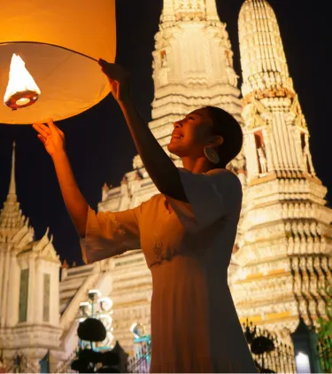 a young couple with travel insurance for Thailand releases a lantern into the sky near Wat Arun temple 