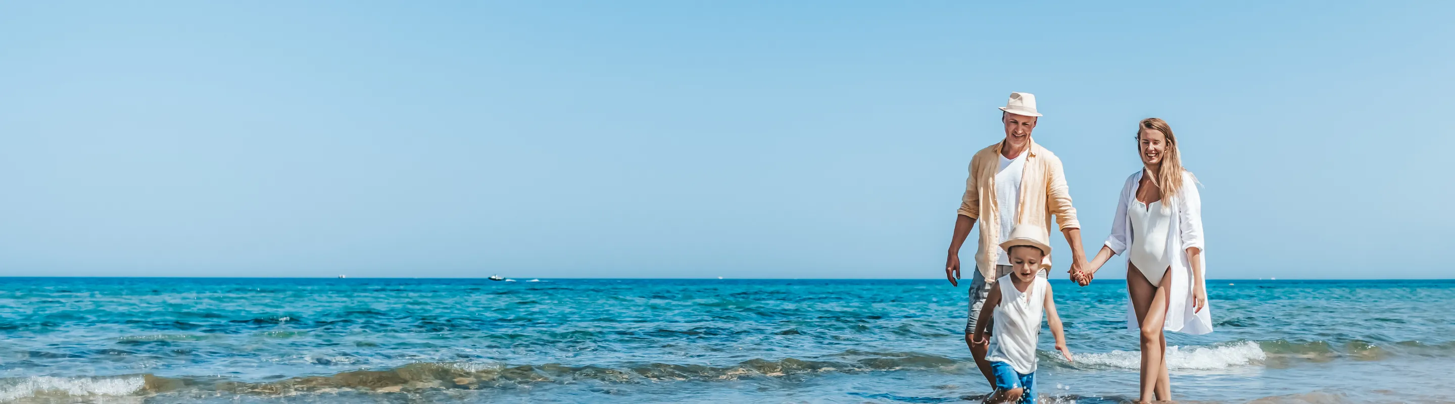 a couple with travel insurance for Egypt walk along the shoreline of an ocean while their son runs ahead