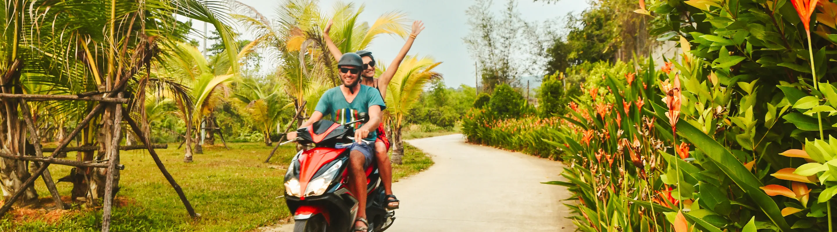 a couple with travel insurance for Vietnam rides a red scooter along a winding road lined with palm trees