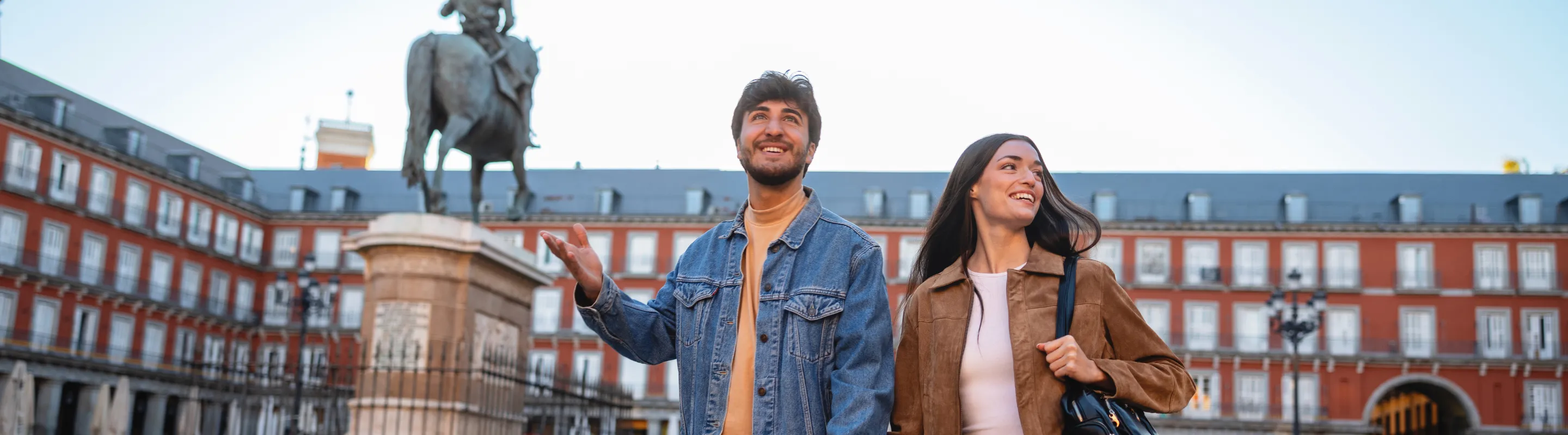 a young couple holds hands as they walk through Paza Mayor in Madrid, insured with travel insurance for Spain