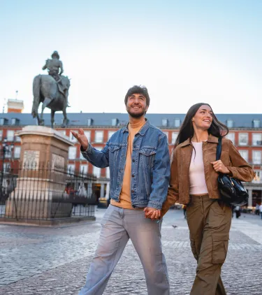 a young couple holds hands as they walk through Paza Mayor in Madrid, insured with travel insurance for Spain