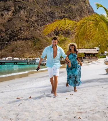 a couple with travel insurance for the Bahamas walks along a white-sand tropical beach with turquoise water