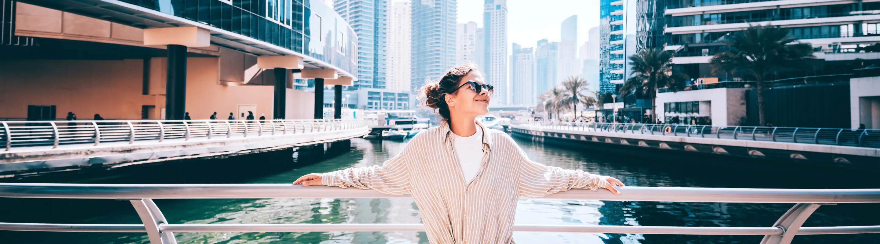 a woman with travel insurance for Dubai stands on a waterfront walkway overlooking the Dubai skyline