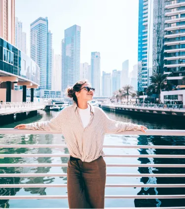 a woman with travel insurance for Dubai stands on a waterfront walkway overlooking the Dubai skyline