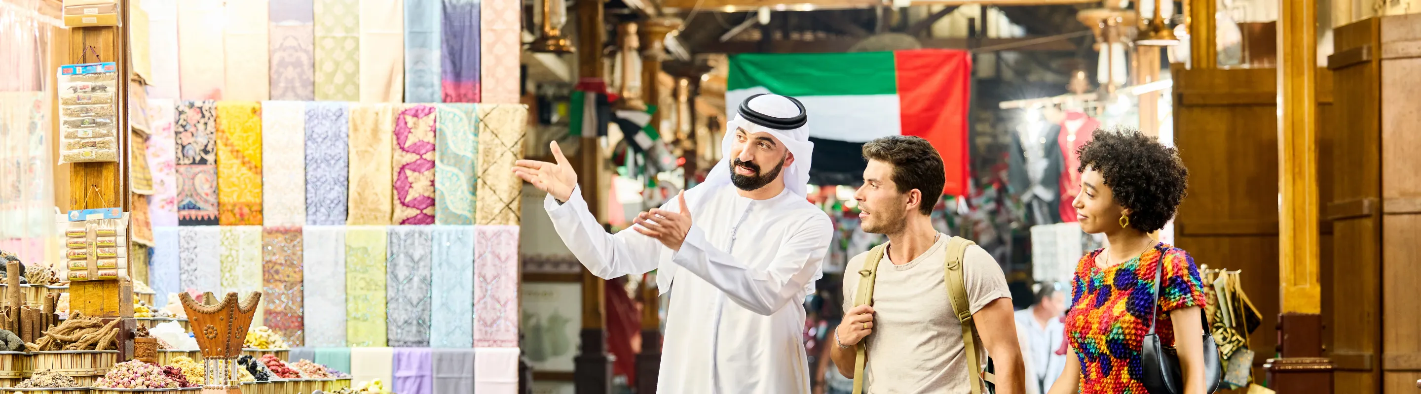 a couple with travel insurance for Dubai explore a traditional market with spice displays and colorful textiles