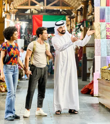 a couple with travel insurance for Dubai explore a traditional market with spice displays and colorful textiles