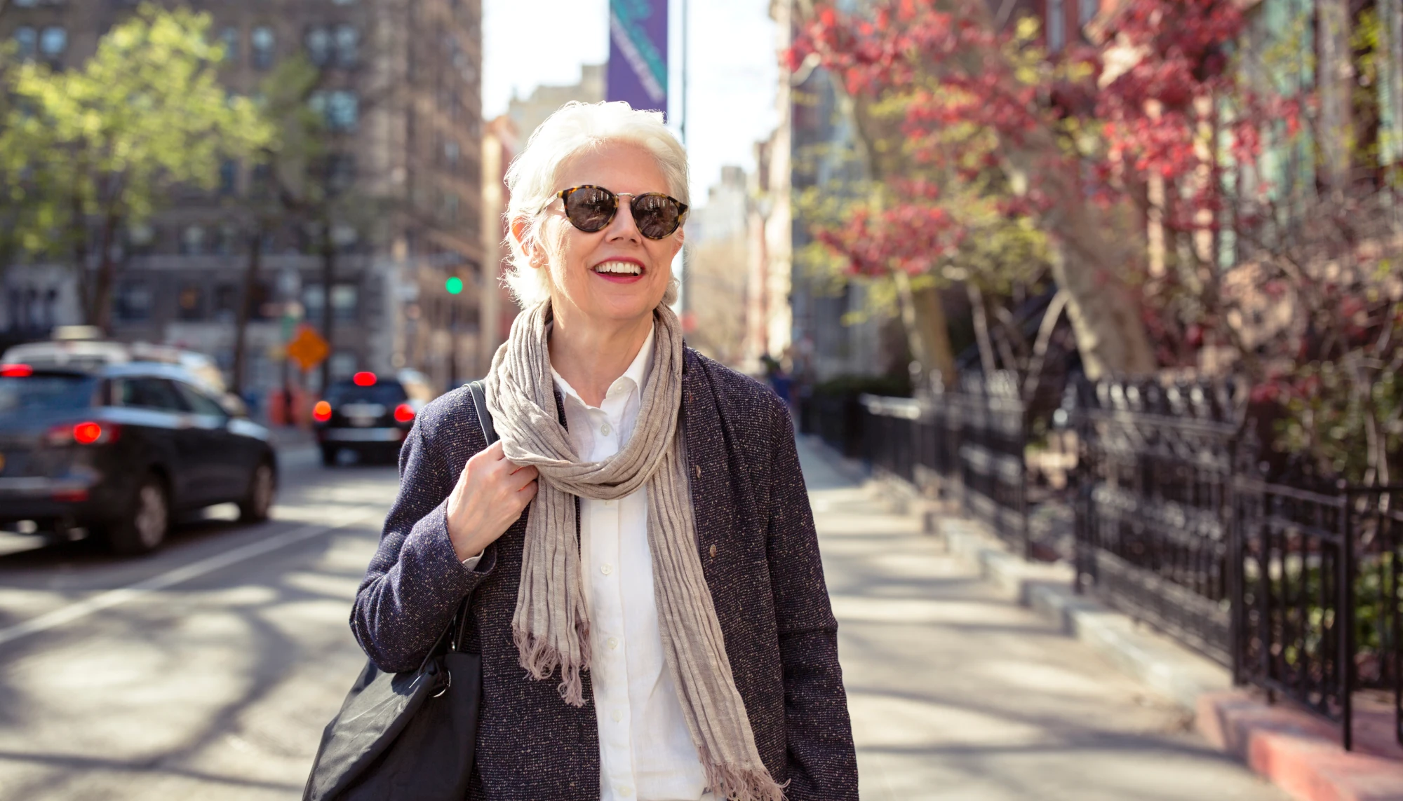 an elderly woman with sunglasses strolls through New York City on vacation after asking, "How much is travel insurance?"