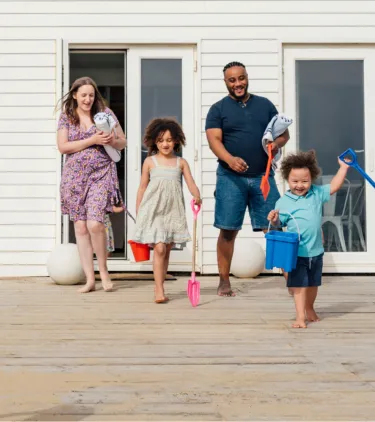 Parents with vacation rental travel insurance heading to the beach with their two young children from the back patio
