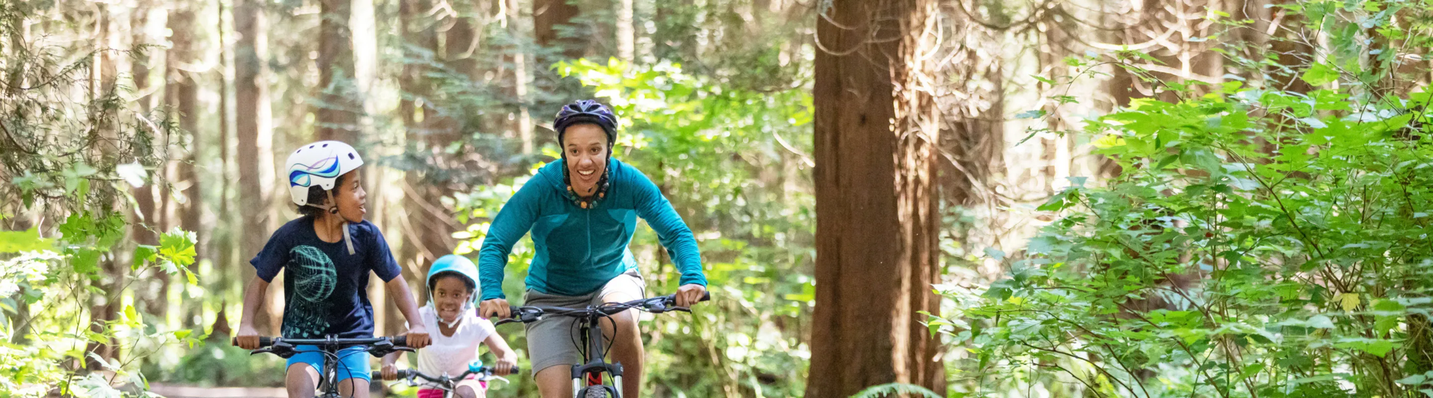 a mother and her two kids bike through a forest trail, enjoying an outdoor adventure with travel assistance available