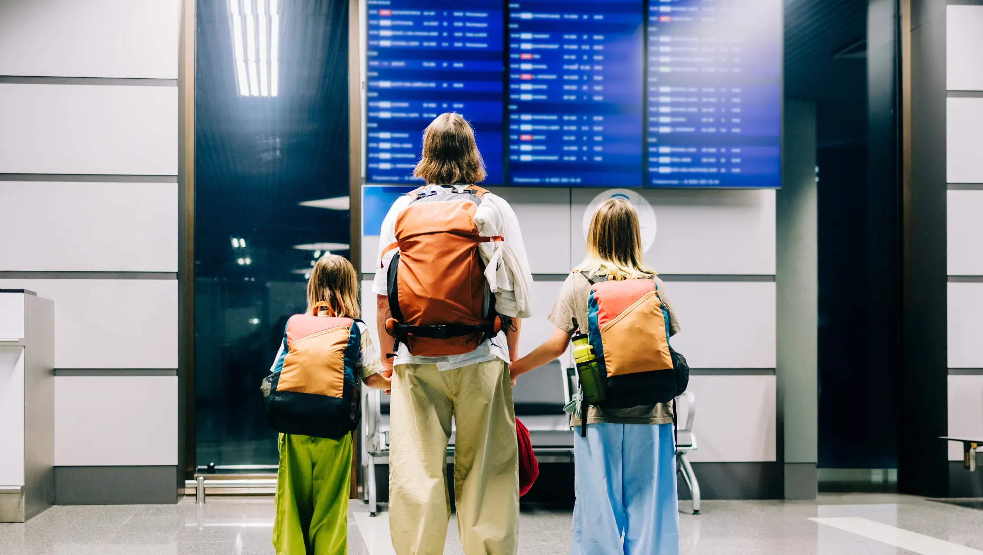 a mother and kids look at the airport departure board, wondering "Does travel insurance cover flight disruptions?"