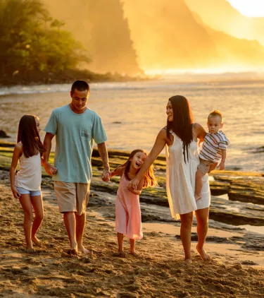 a family of five walks on the beach at sunset, insured with travel insurance for Hawaii
