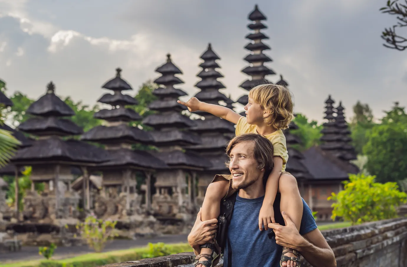 a father holds his son on his shoulders as they walk through a temple, insured with travel insurance for Bali