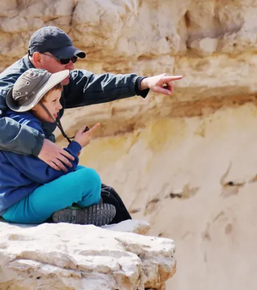 a father and child sit down to enjoy views on a desert hike, insured with travel insurance for Israel 