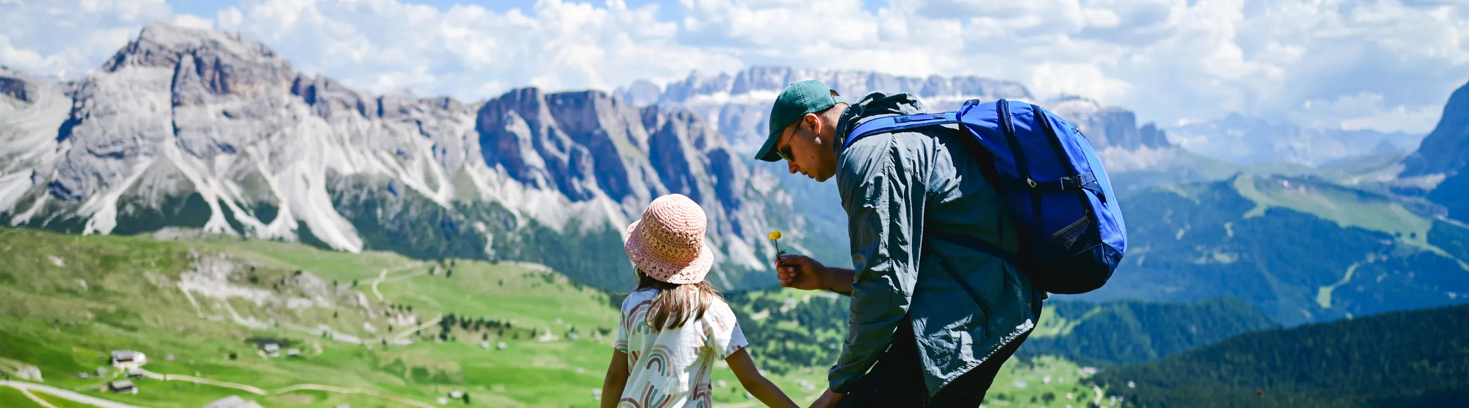 a father with travel insurance for Italy shows his daughter a flower as they hike the Italian Dolomites 