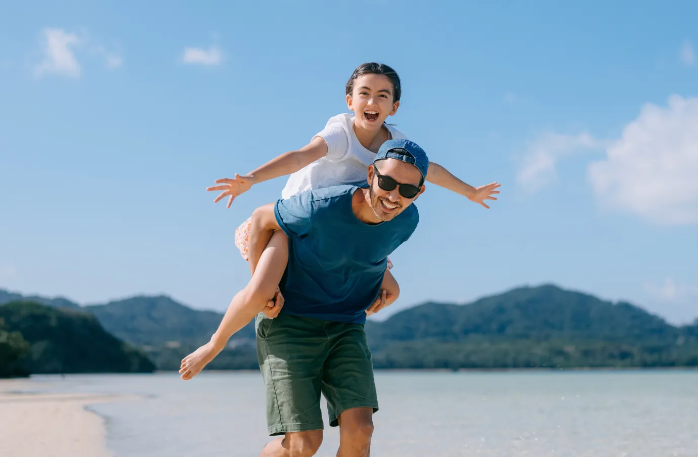 a father gives his daughter a piggyback ride along a sunny tropical beach